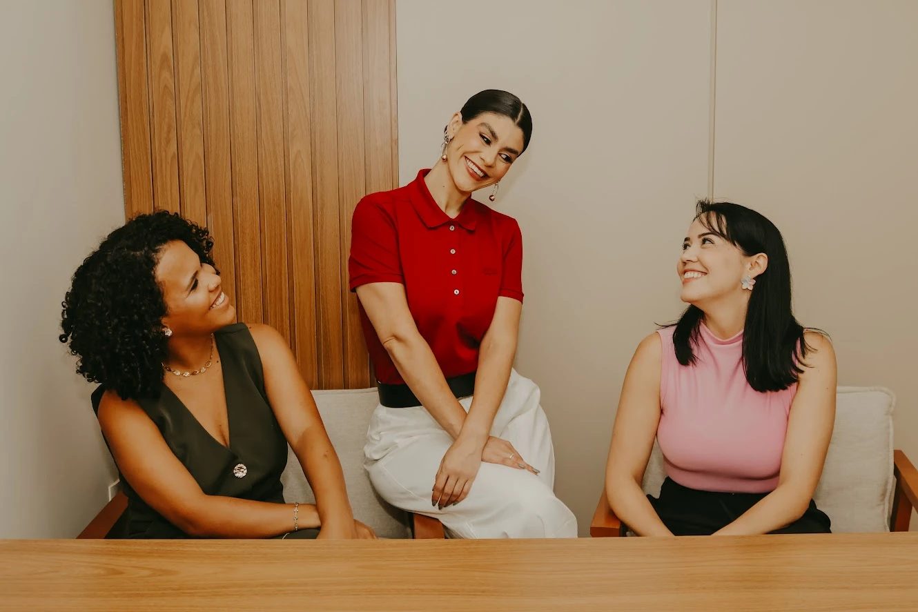 As três profissionais do Espaço Desenvolvimento Pleno sentadas juntas e sorrindo: Jennifer Barbosa, Amanda Pinheiro e Graciele.